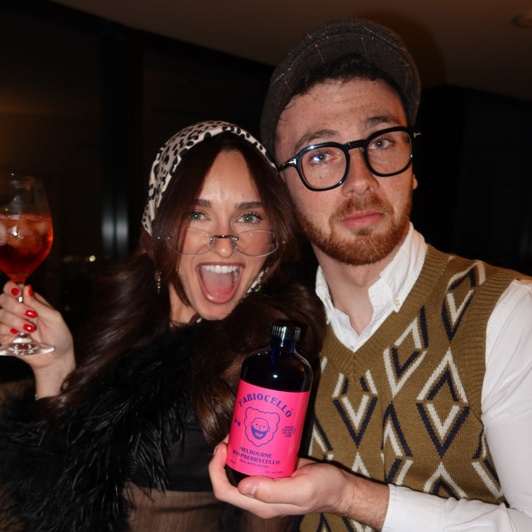 Two people posing with a pink bottle on a patterned rug.